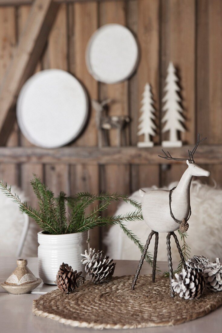 Festive table arrangement; animal figurines and fir cones on woven place mat and white ceramic vase of fir branches