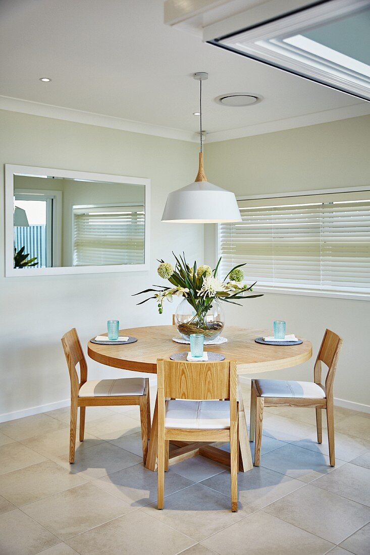 Round wooden table and chairs below pendant lamp with white lampshade in dining room