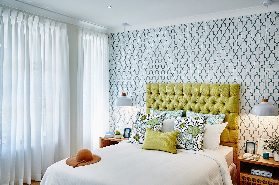 Bedroom with double bed, yellow upholstered headboard, scatter cushions and retro wallpaper