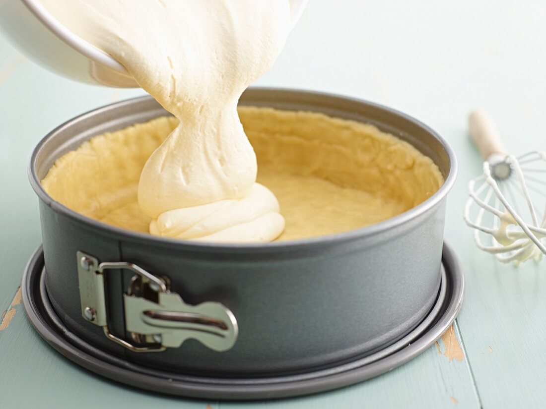 Cheese mixture for a cheesecake being poured into a baking tin lined with pastry