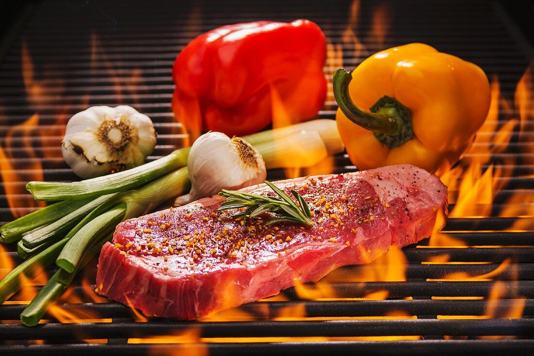 Beef steak with rosemary, red and yellow peppers, fresh garlic and spring onions on a flaming barbecue