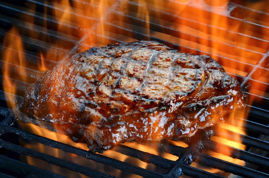 A ribeye steak on a flaming barbecue