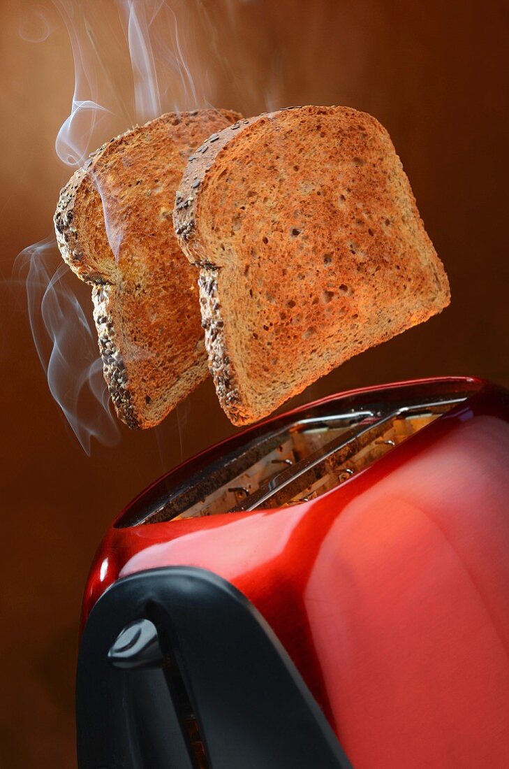 Smoking wholemeal toast jumping out of a red toaster