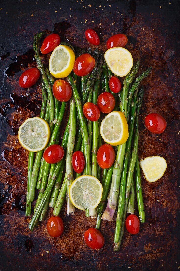 Asparagus, lemon slices and organic grape tomatoes with olive oil and spices on a baking tray
