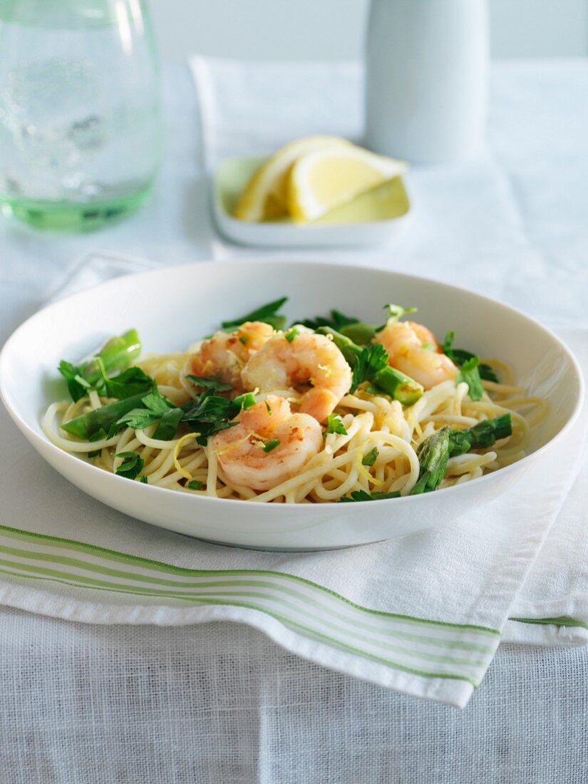 Spaghetti with prawns, asparagus and fresh parsley on a table with lemon slices and water