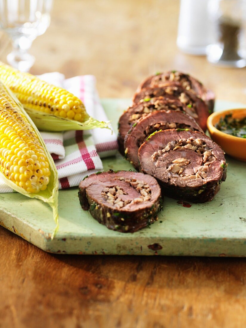 Steak roulade with chopped mushrooms, herb sauce and grilled corn cobs