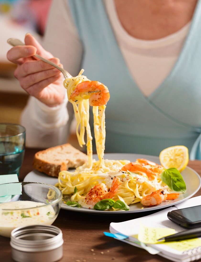 Frau isst Bandnudeln mit würzigen Garnelen zum Lunch