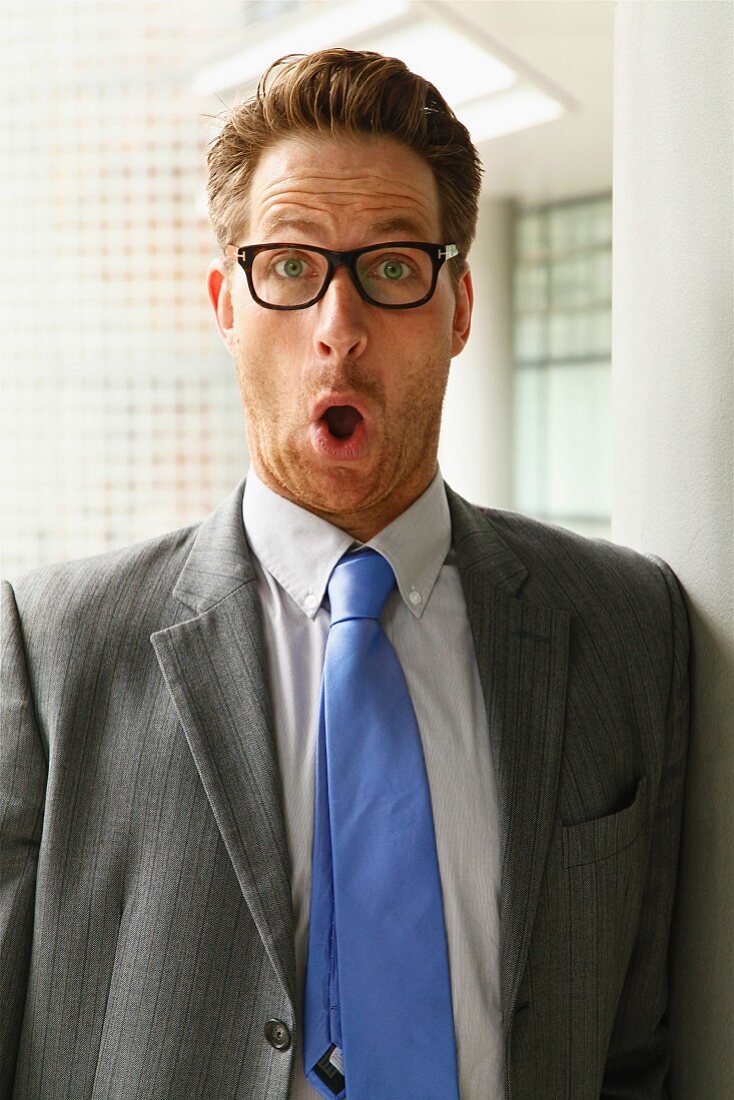 A man wearing glasses wearing a grey blazer and a tie making a face - surprised or indigent