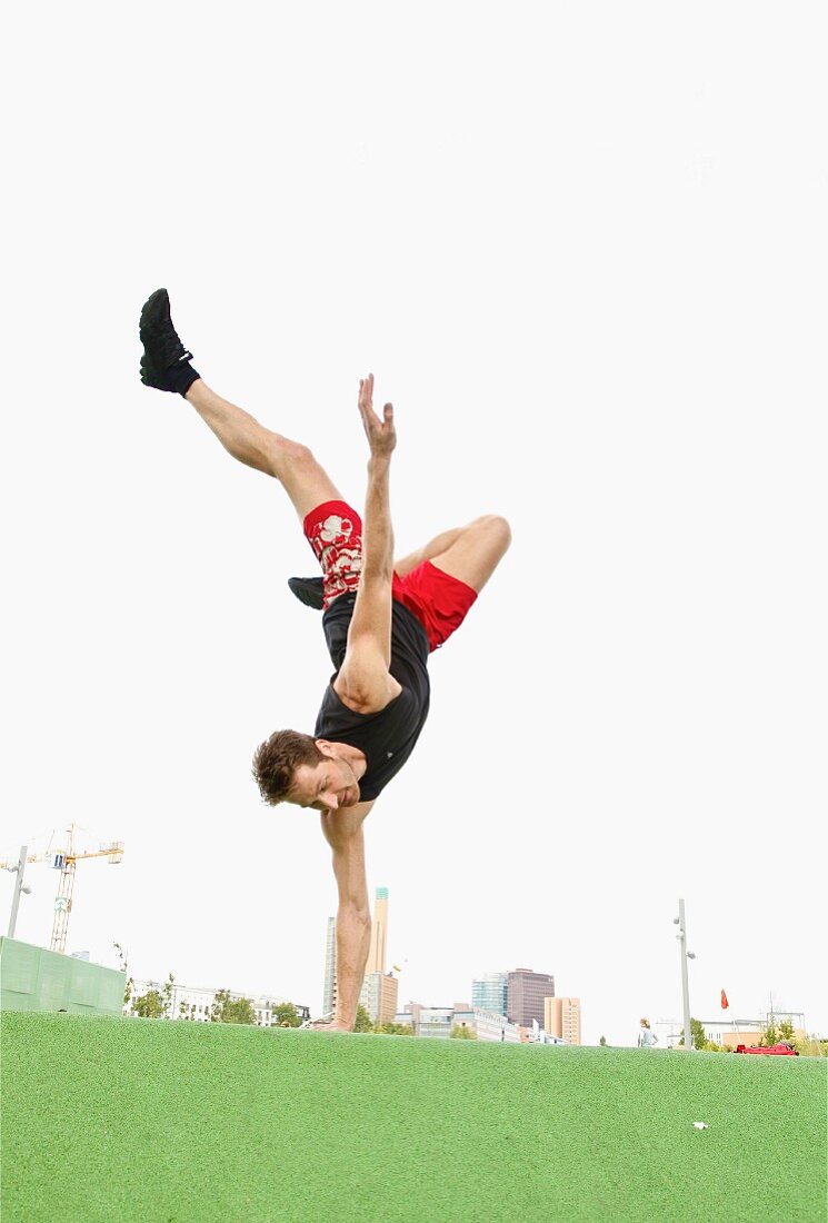 A man performing a one-handed handstand on grass against a skyline