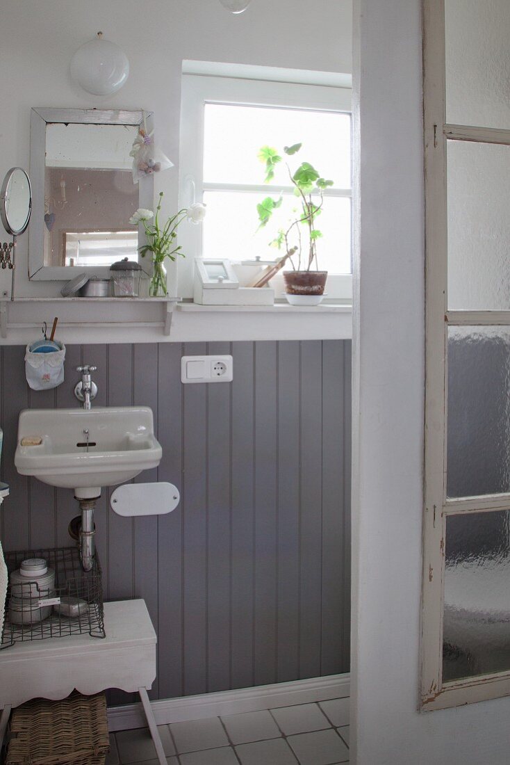 Kleines Bad mit halbhoher, grauer Holzvertäfelung, seitlich ein altes Fenster als Duschabtrennung