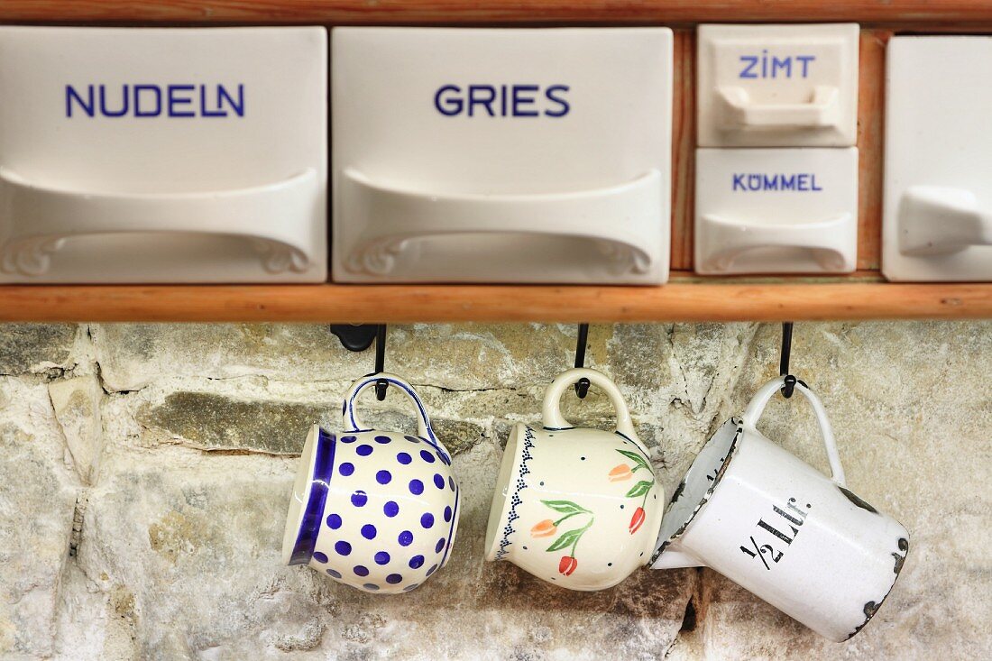 Labelled china scoops and vintage cups hung from hooks against stone wall