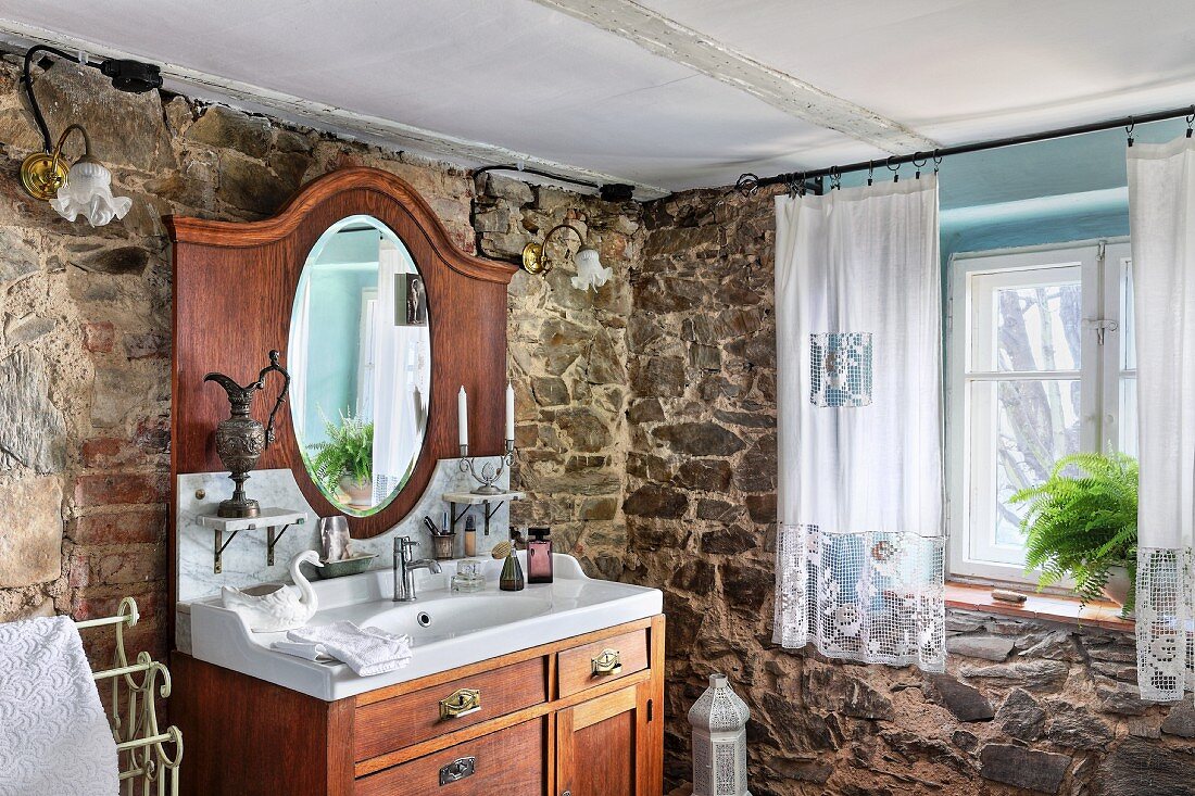 Massives Waschtischmöbel mit Spiegelaufsatz in rustikaler Badezimmerecke mit Natursteinwänden