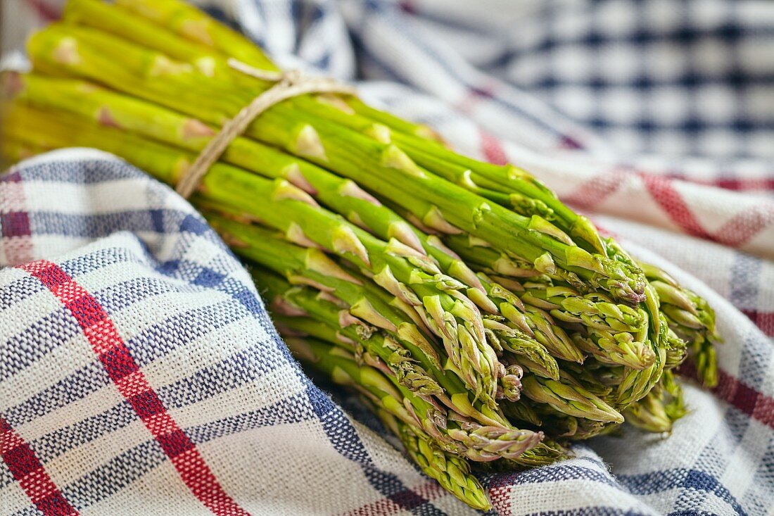 A bunch of green asparagus on a checked tea towel