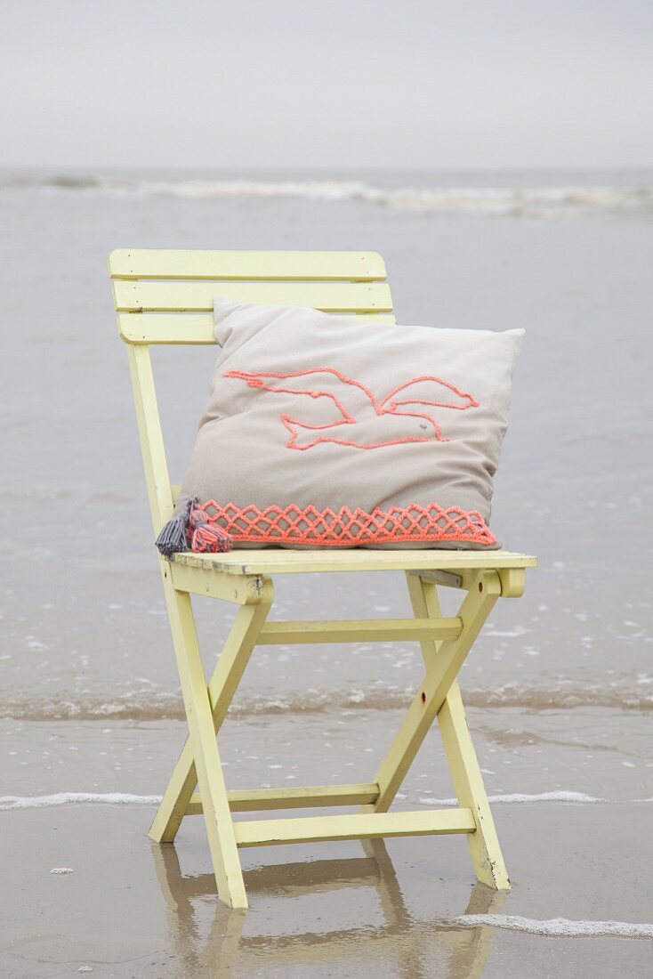 Cushion with crocheted seagull motif on wooden chair on beach