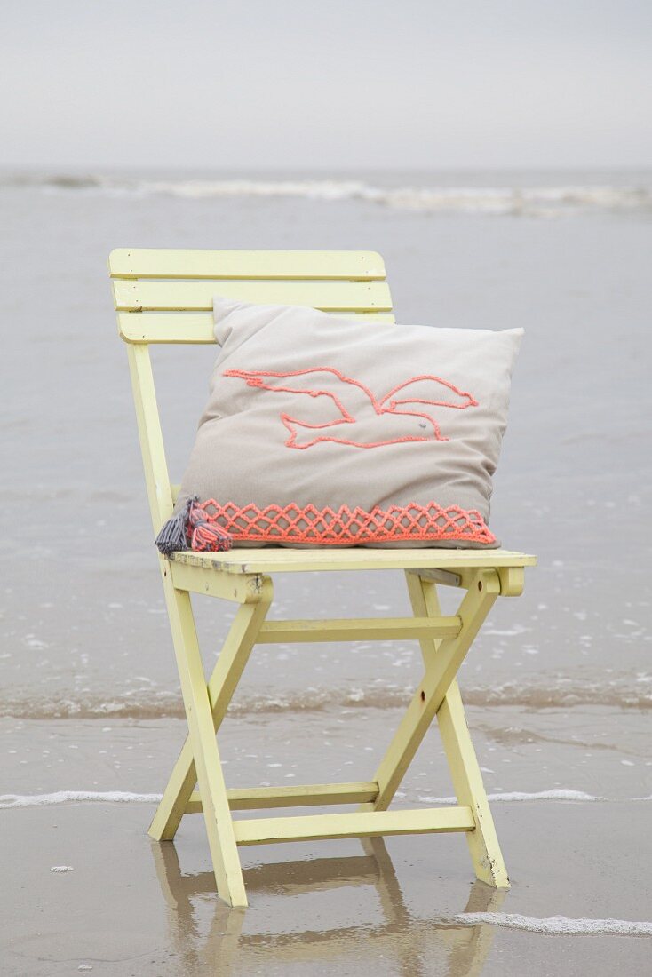 Kissen mit gehäkeltem Möwenmotiv auf Holzstuhl am Strand