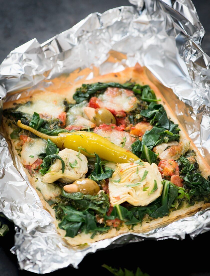 A slice of pizza with spinach, artichokes and stuffed olives