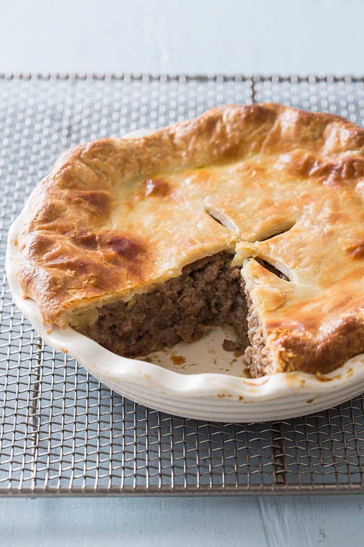 Tourtiere (French-Canadian meat pie) in a baking dish on a wire rack with a slice cut out