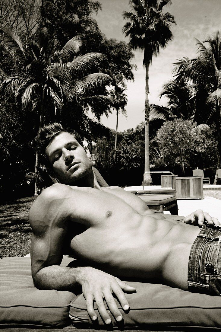 Junger Mann entspannt sich in der Sonne am Pool, im Hintergrund Palmen