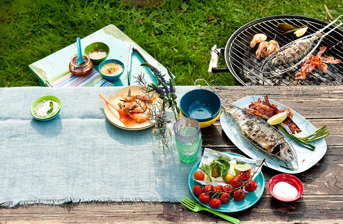 A barbecue in the garden with food on the barbecue and on the table