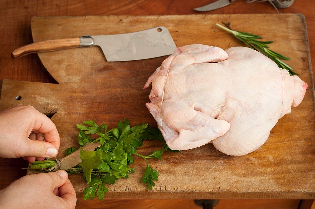 A woman tying a bouquet of herbs next to a raw chicken