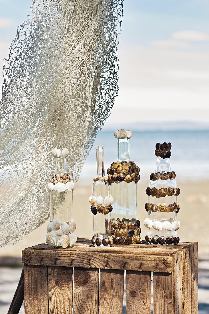 Glasflaschen dekoriert mit Muscheln auf Holzkiste am Strand