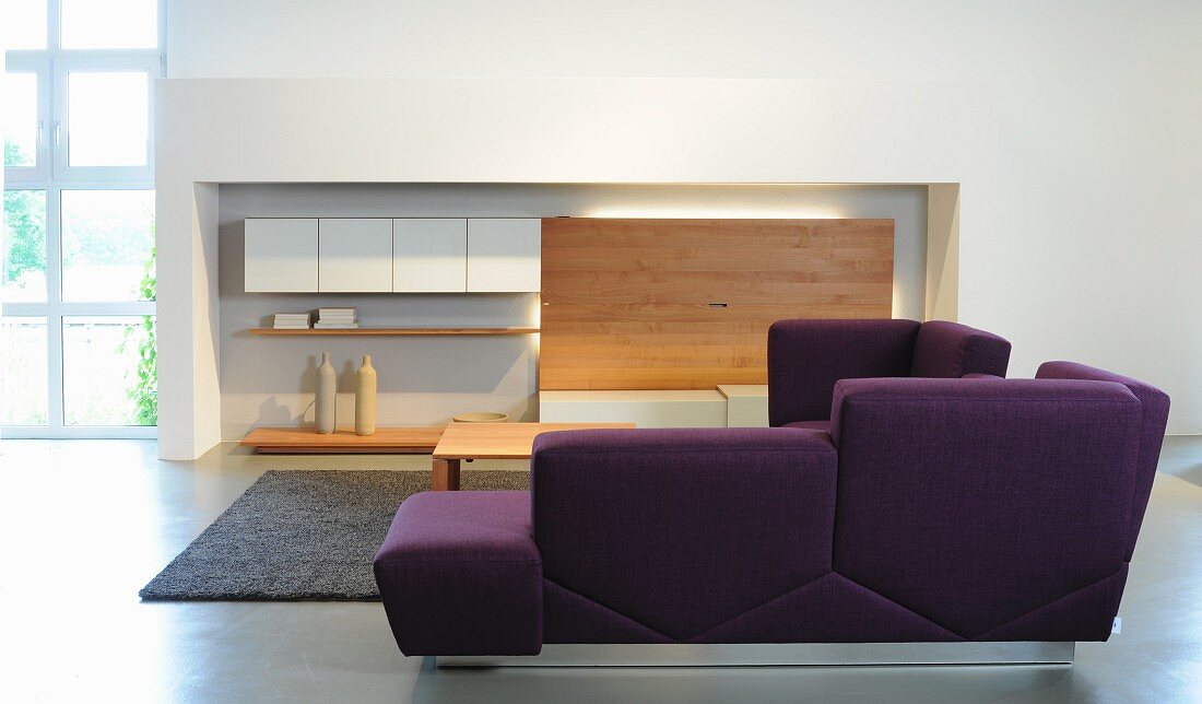 Purple corner sofa in front of wall-mounted cabinet in niche in contemporary lounge area