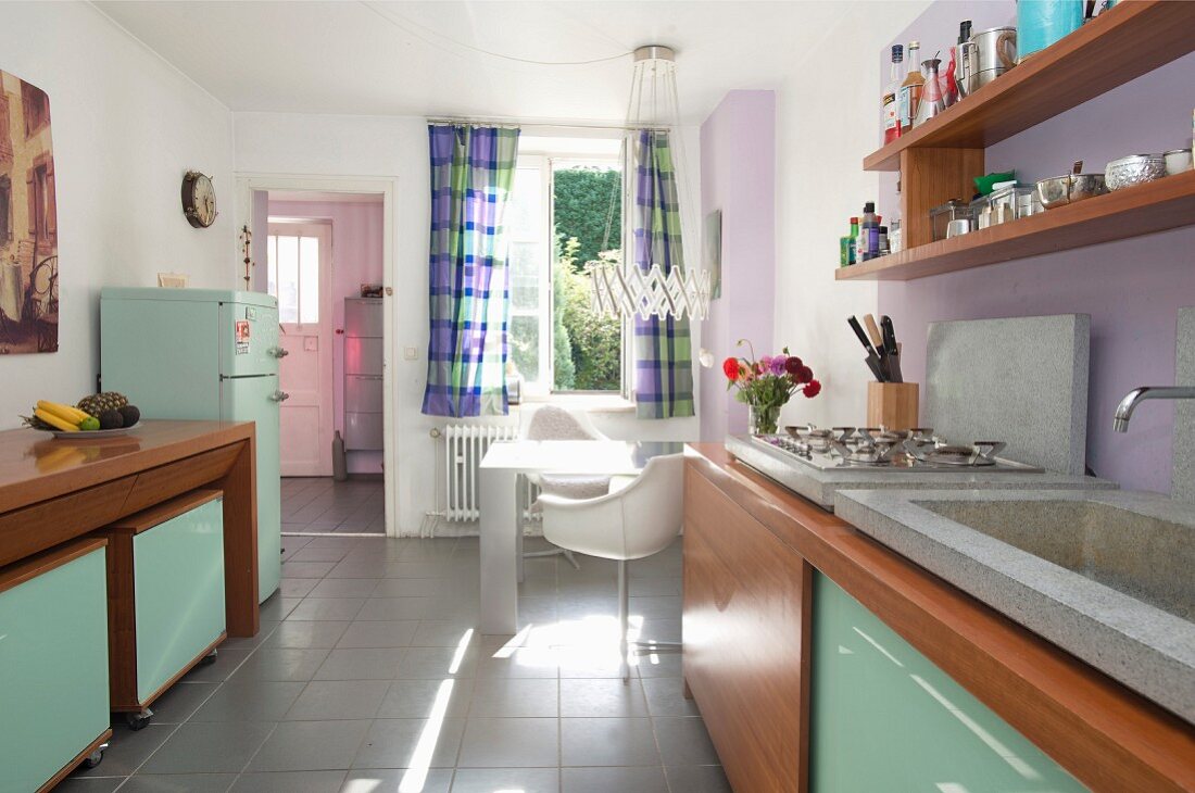 Retro kitchen; wooden cabinets with mint-green glass doors and dining area below window in background