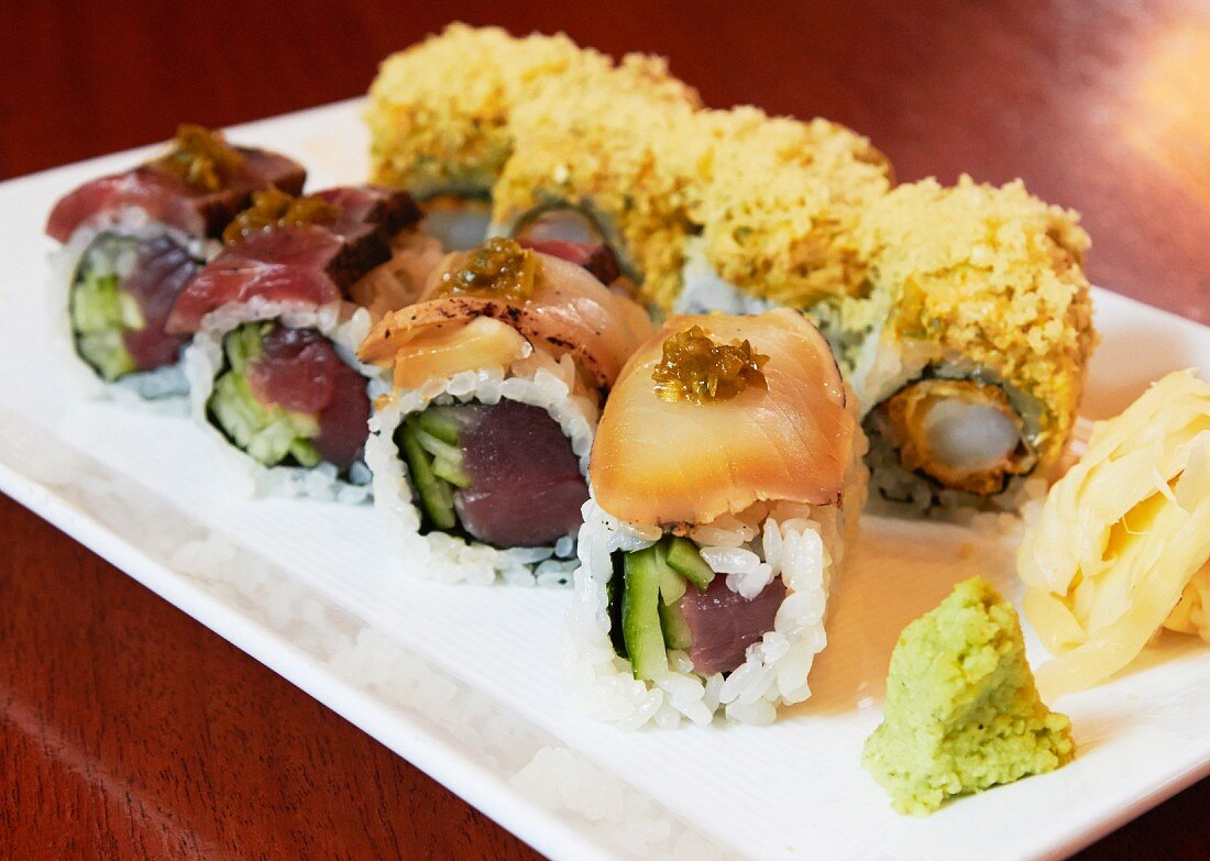 Various types of sushi with wasabi and ginger on a serving platter