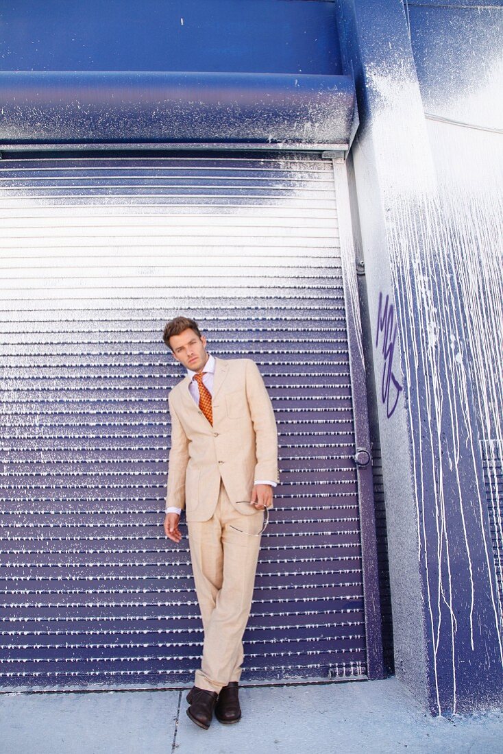 Young man standing in front of a metal door wearing a light suit