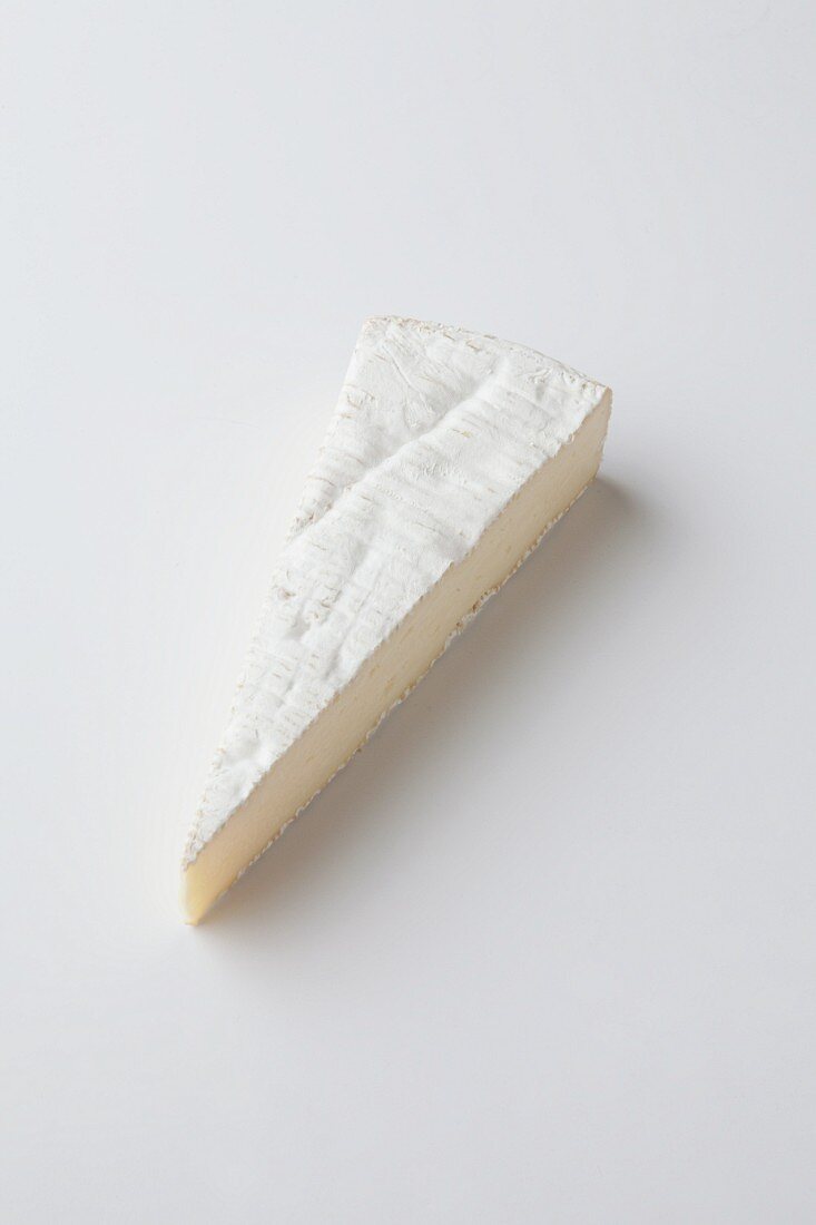 A slice of Brie de Meaux on a white surface