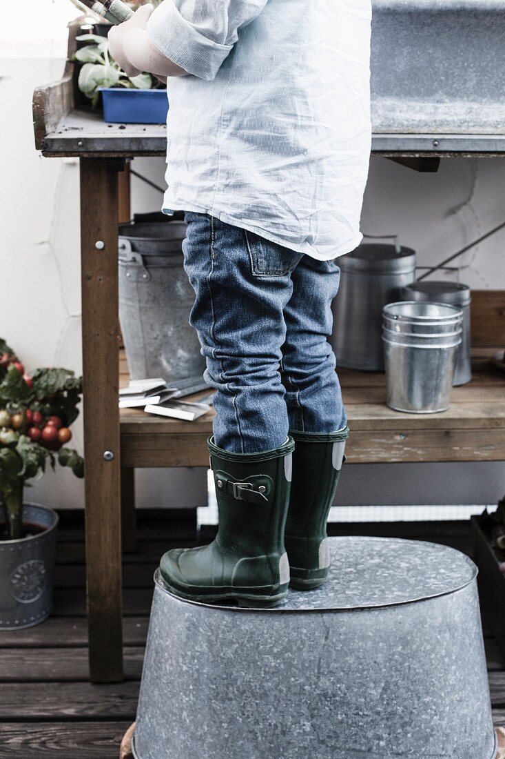 Boy standing on upturned zinc tub at potting bench on balcony