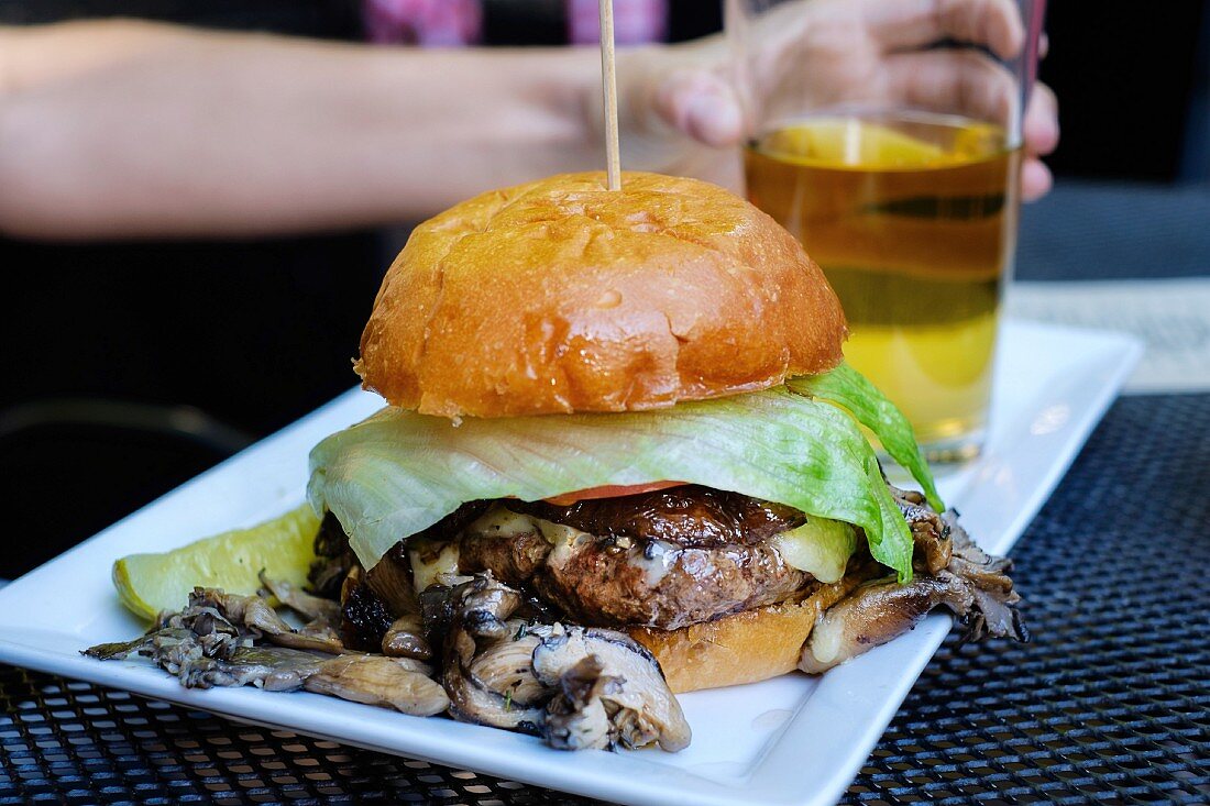 A burger with mushrooms with a glass of beer on a serving platter