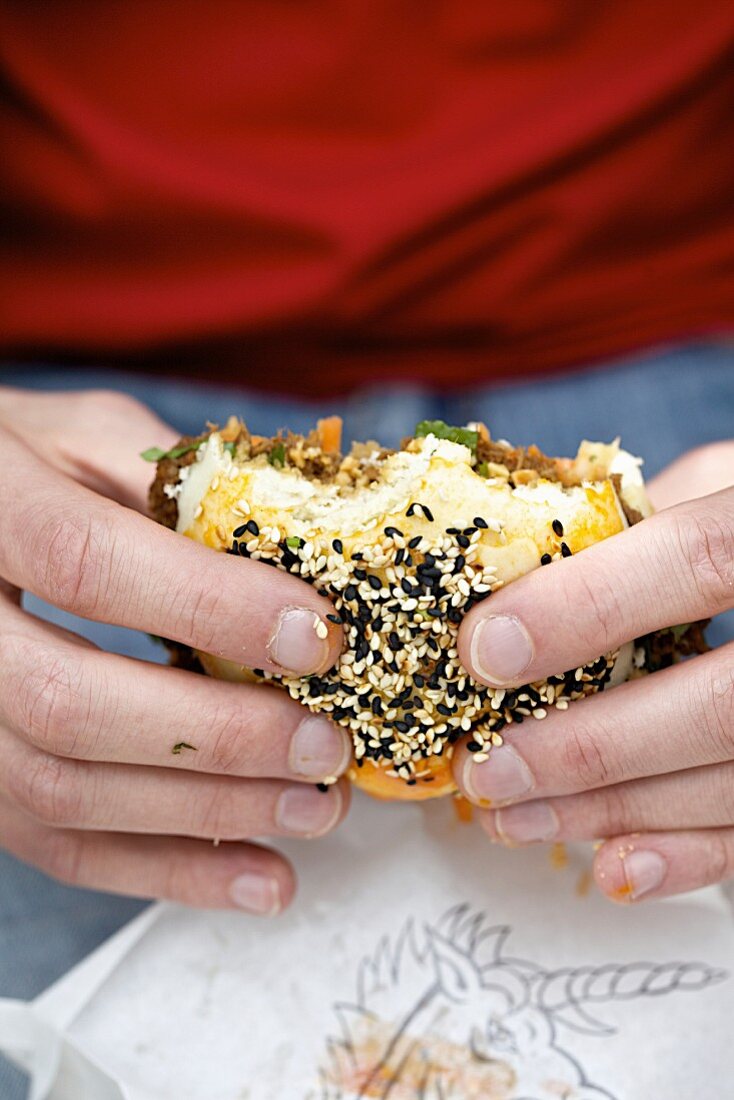 A person holding a Gua Bao burger with sesame seeds (oriental street food)