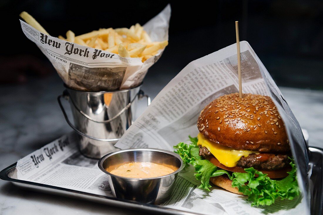 Hamburger mit Pommes & Dip in Zeitungspapier gewickelt auf Tablett