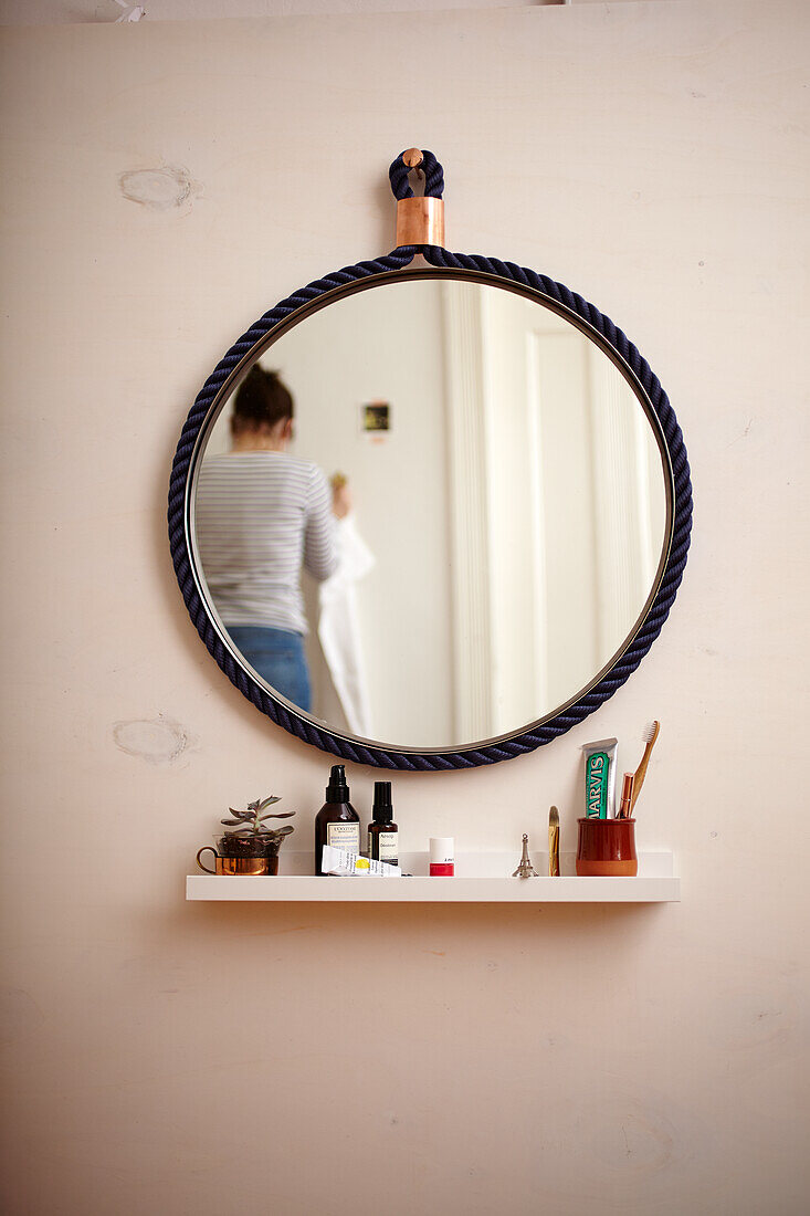 Round wall mirror with rope frame above floating shelf in bathroom