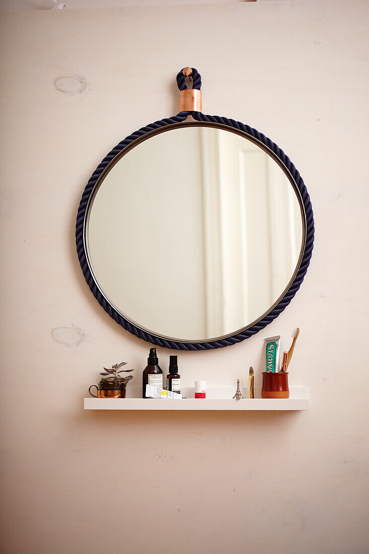 Round mirror with blue rope frame above floating shelf in bathroom