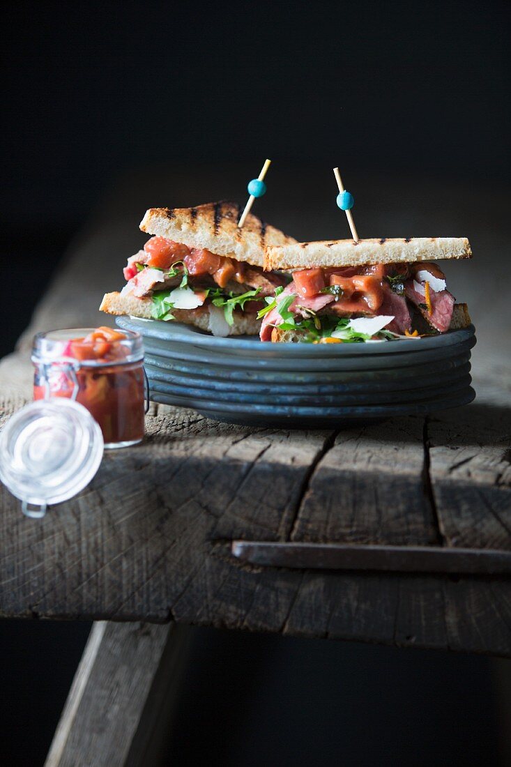 A toasted sandwich with grilled steak and rhubarb chutney on a wooden table