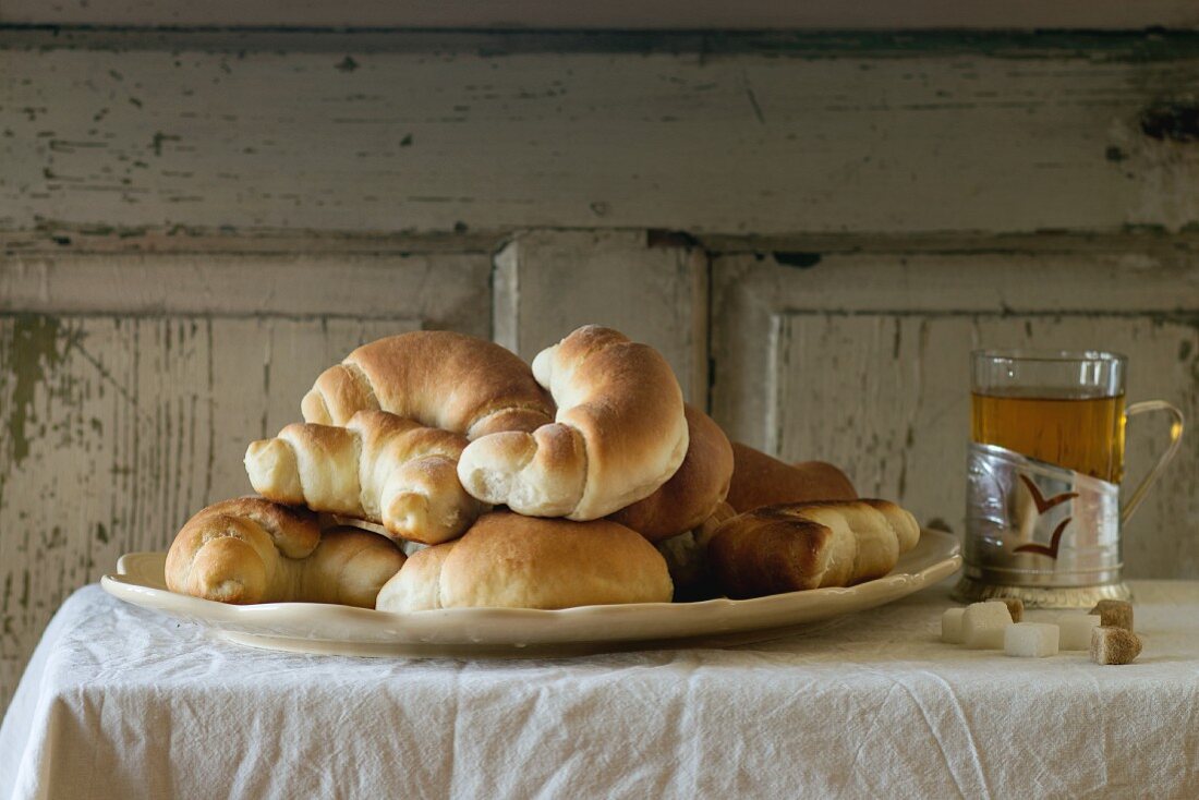 A plate of freshly baked homemade crescent rolls, served with a cup of tea on a white tablecloth