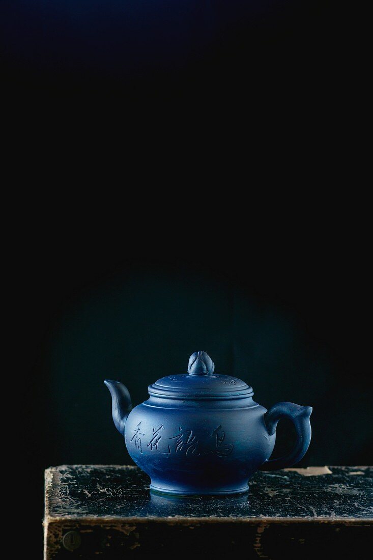 Blaue Keramikteekanne vor schwarzem Hintergrund