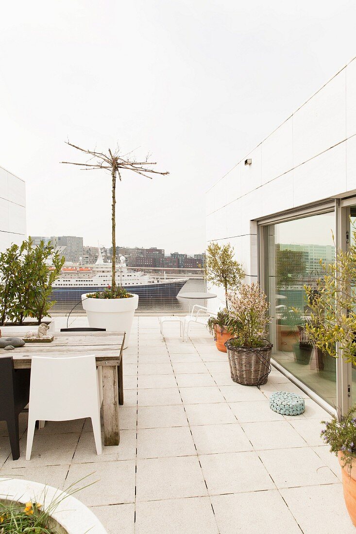 Terrasse mit hellem Steinboden, seitlich moderne Outdoorstühle am verwittertem Holztisch, im Hintergrund vorbeifahrendes Passagierschiff