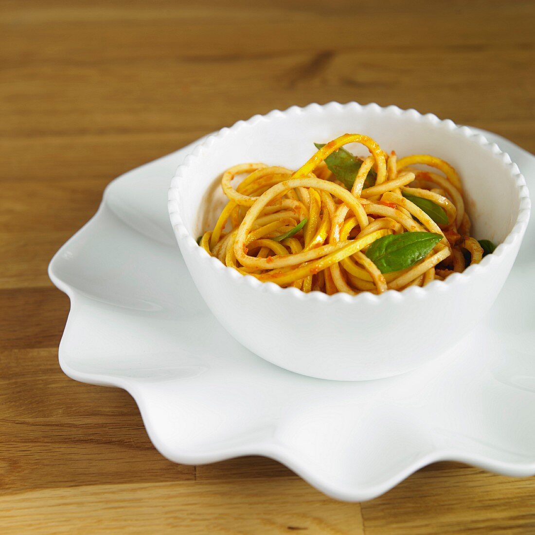 Gelbe Zucchinisppaghetti mit Tomatensauce und Basilikum in weisser Schale