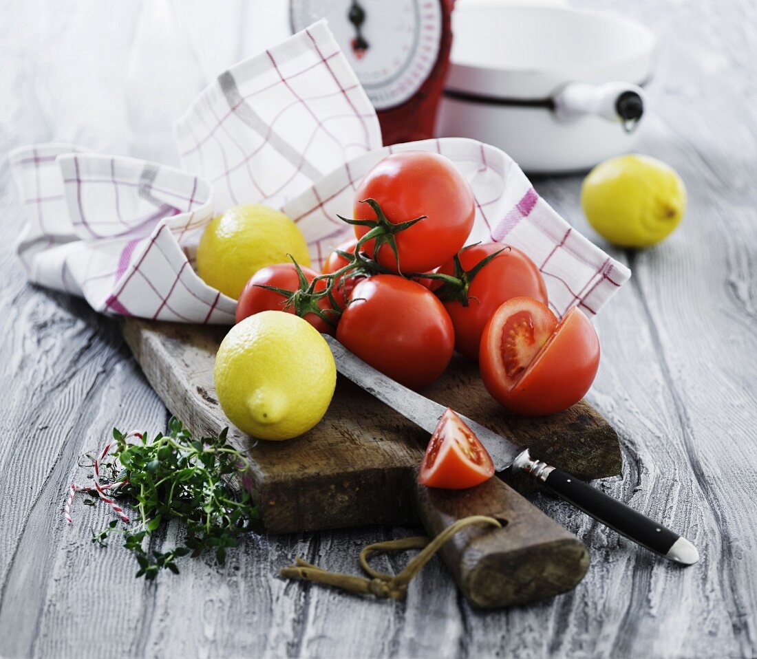Fresh tomatoes, lemons and herbs on a chopping board in front of a pair of kitchen scales