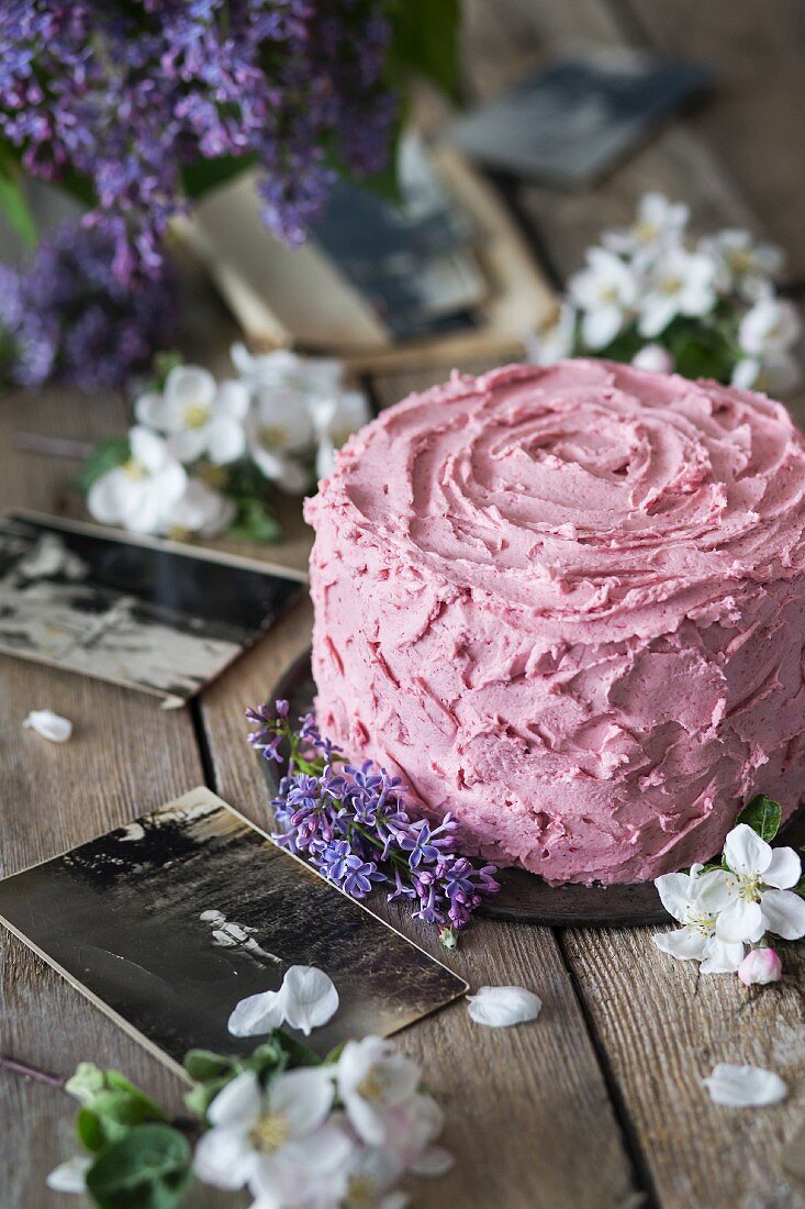 Frühlings-Geburtstagskuchen mit rosa Zuckerguss auf Holztisch mit Blumen und alten Fotografien