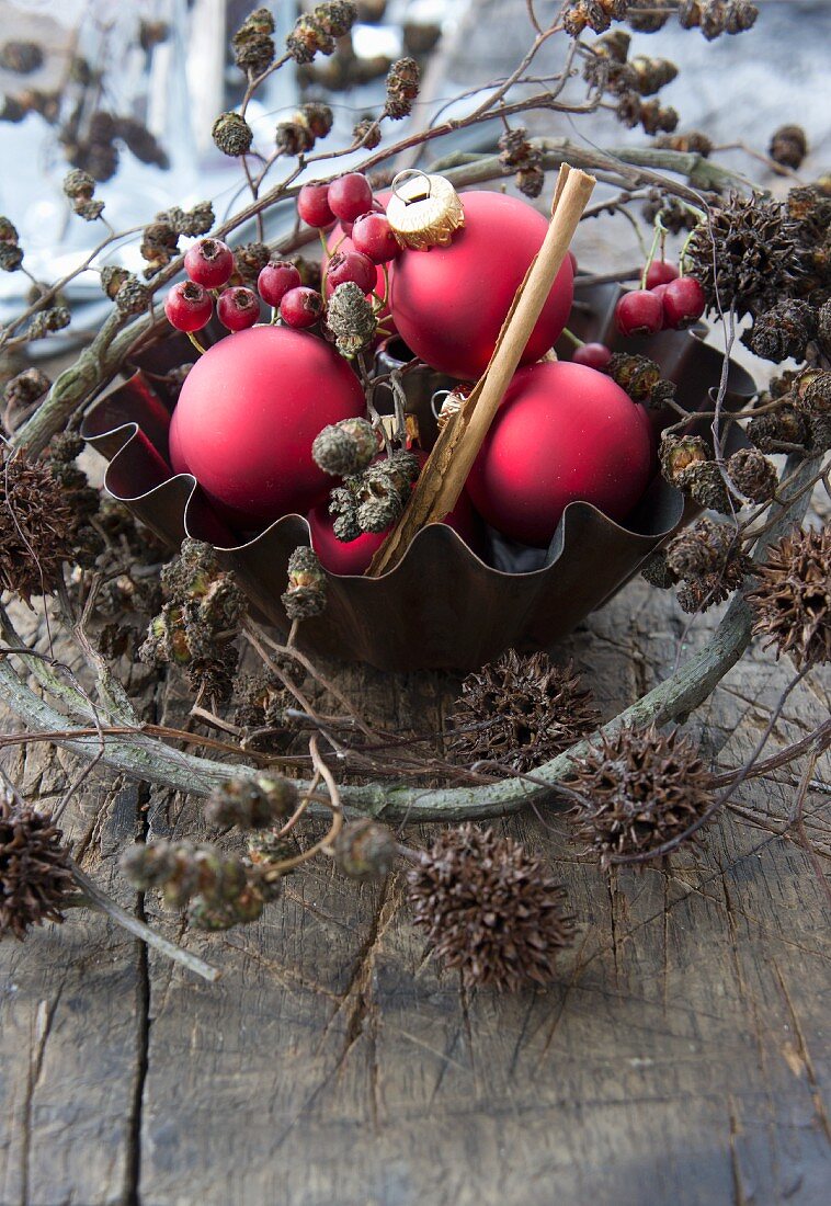 A baking tin with red Christmas tree baubles, hawthorn berries, alderberry sprigs and maple berry sprigs