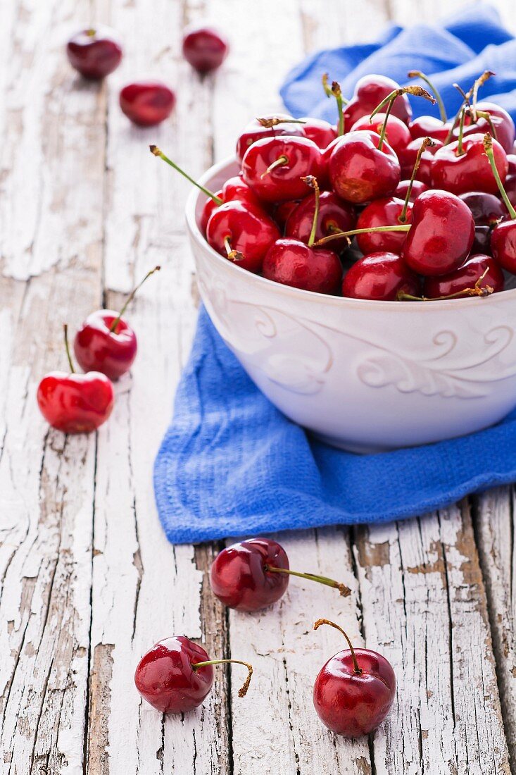 A bowl of fresh cherries on a blue cloth on a weathered wooden table