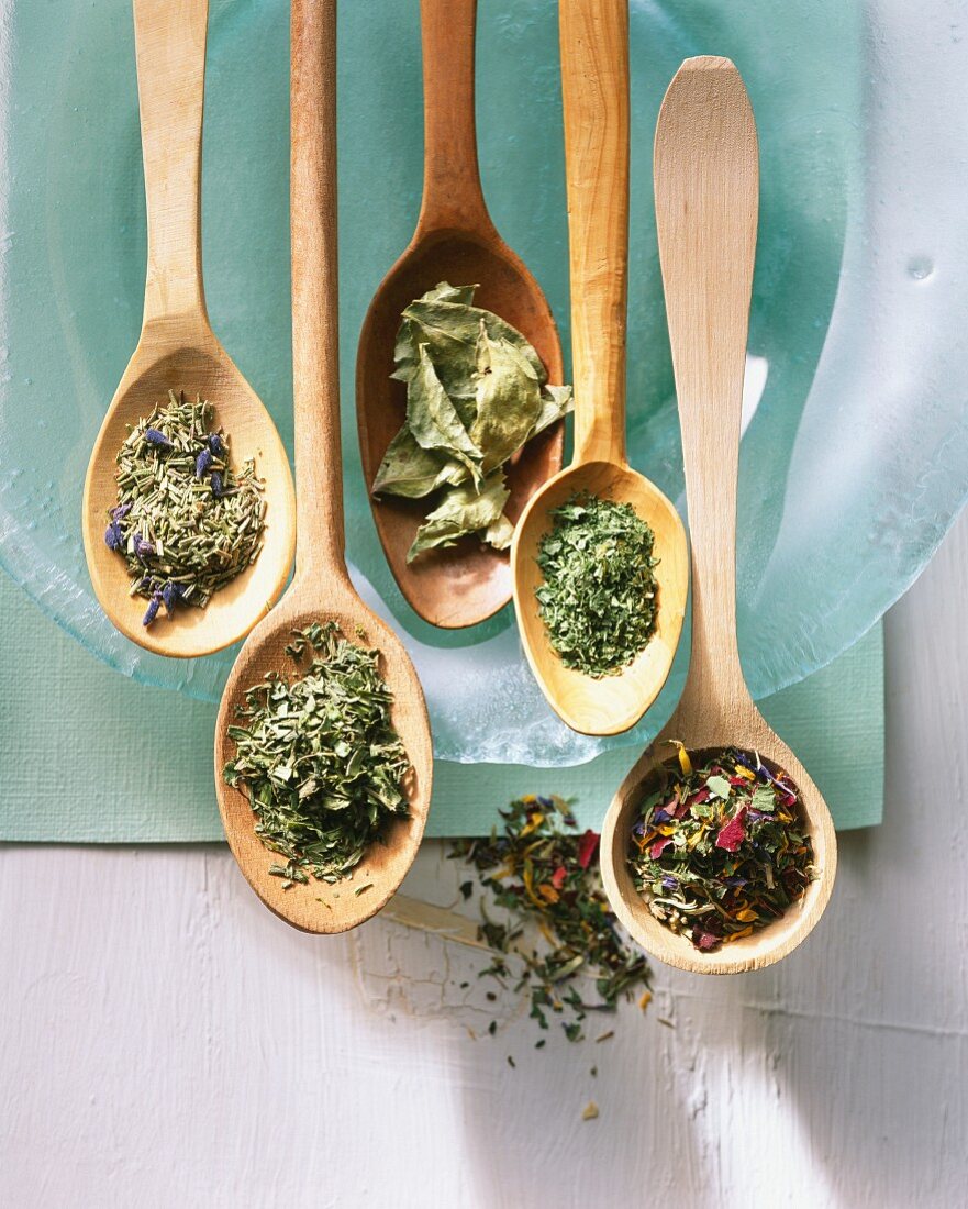 Various dried herbs and loose leaf tea on wooden spoons
