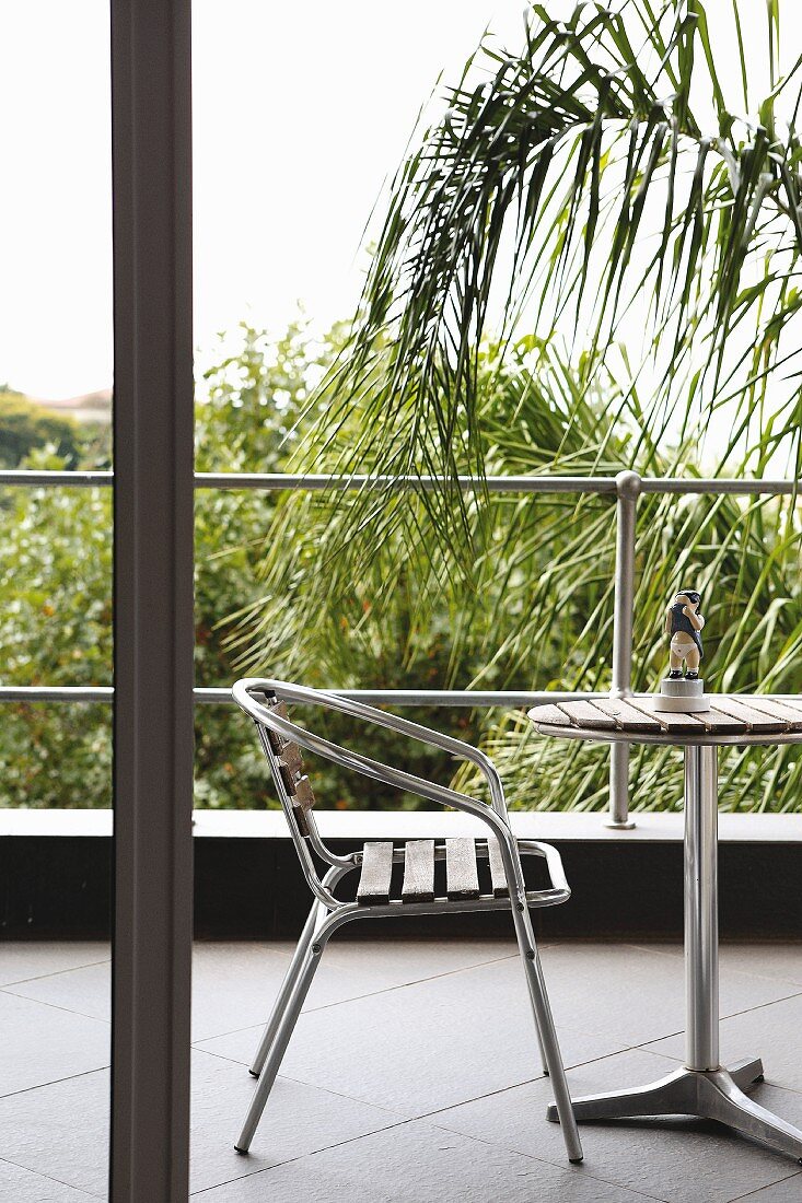 Chair and table made from tubular metal and wooden slats on balcony with palm trees in background