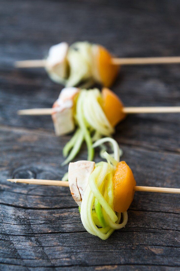 Skewers with rolled courgette noodles, peaches and cheese on a wooden surface