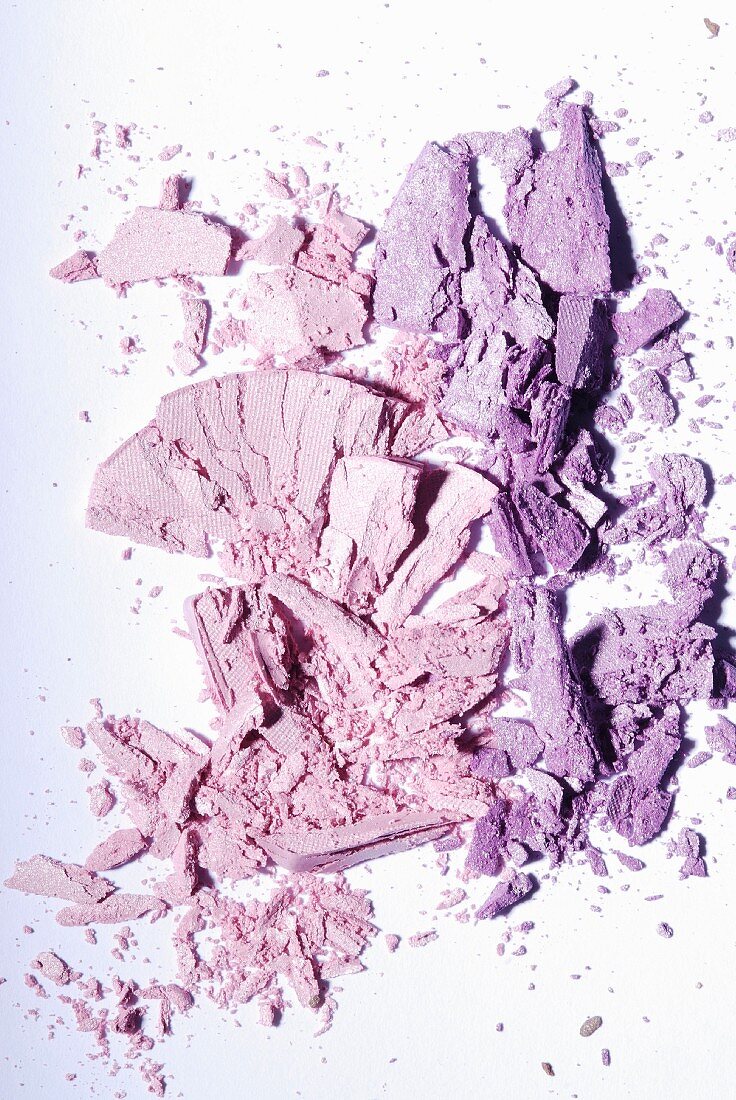 Two shades of purple eye shadow crumbled on a white surface