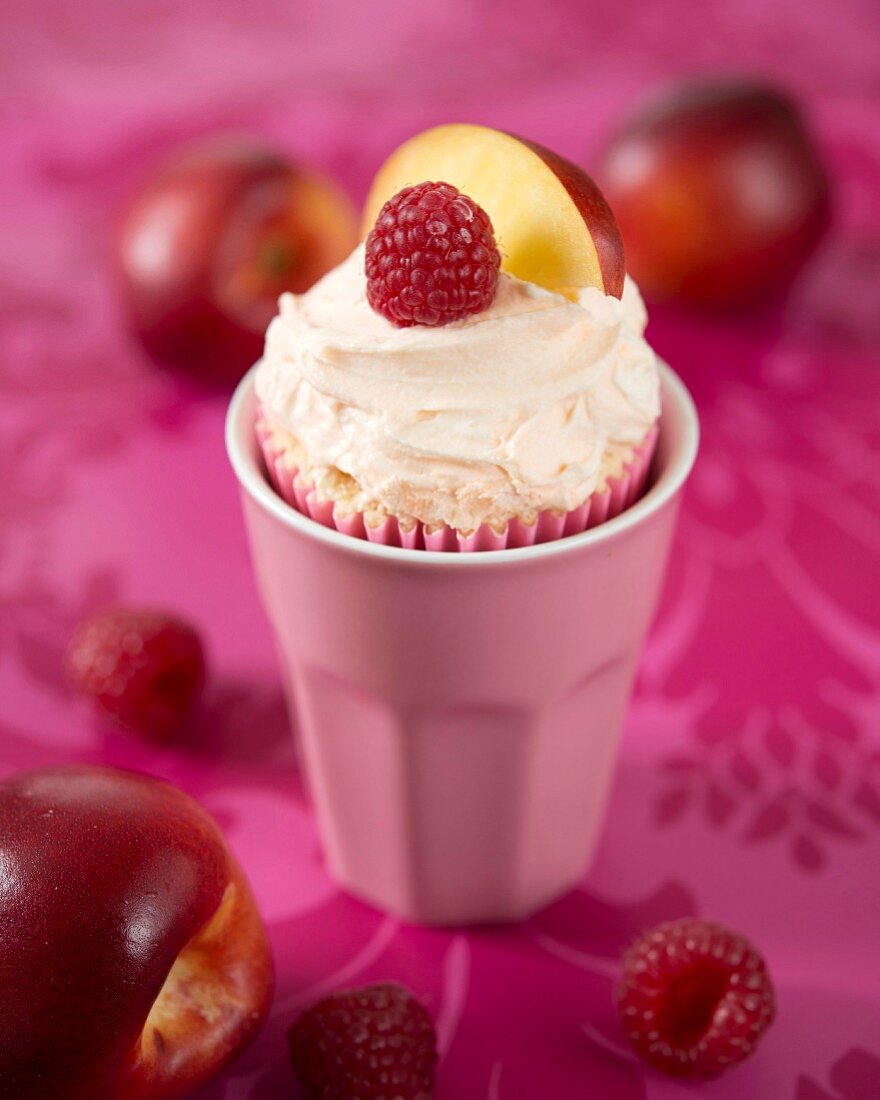A peach melba cupcake with fresh peaches and raspberries